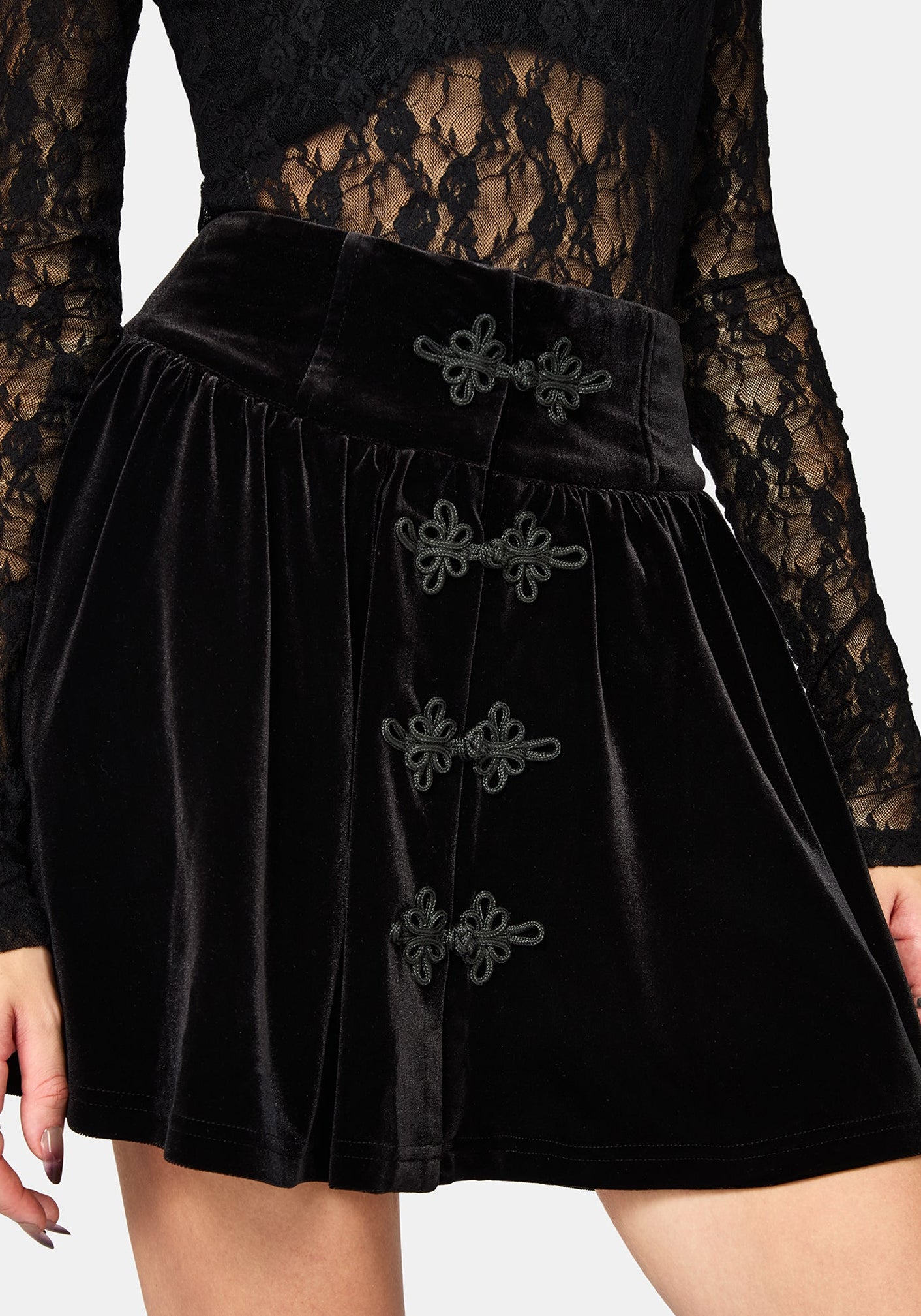 Black velvet mini skirt with decorative dark gray bow accents down the front, shown on a model against a light gray background.