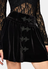 Black velvet mini skirt with decorative dark gray bow accents down the front, shown on a model against a light gray background.