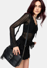Woman wearing a black lace mesh top with long sleeves holding a black handbag on a plain background 