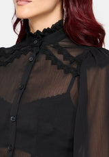 Close-up of a model wearing a black sheer long-sleeve blouse with a ruffled high collar and black lace trim details.