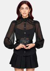 A woman modeling a black long-sleeve blouse with sheer mesh sleeves, a high ruffled collar, and a sheer yoke panel, paired with a matching pleated black skirt and a black belt with silver hardware, against a light gray background.