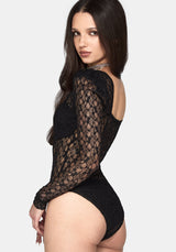 A woman modeling a black lace long-sleeve bodysuit from the back, showing the open back and sheer floral lace pattern, against a light gray background.