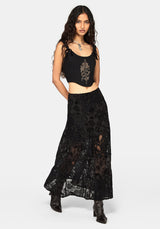 A model wearing a black sleeveless corset top with gold embroidery and a matching black lace maxi skirt, paired with black ankle boots, against a light gray studio background.