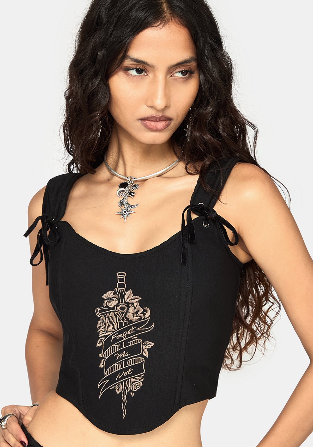 A woman wearing a black sleeveless corset with side tie details and a beige graphic print on the front, photographed against a light gray studio background.