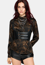 A model with dark red hair wearing a black and brown floral patterned long-sleeve blouse with a black faux-leather corset-style waist belt, layered silver necklaces, and black faux-leather shorts, set against a plain light gray background.