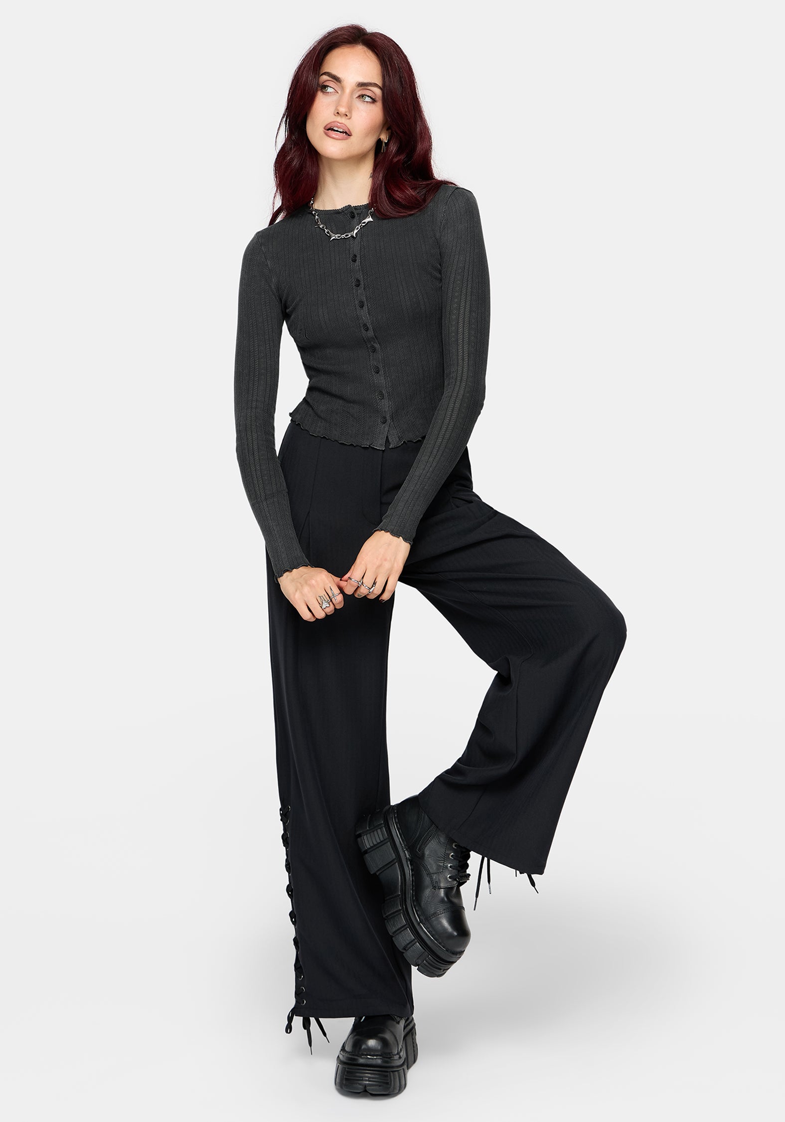 A woman modeling a dark gray ribbed long-sleeve button-front top paired with black wide-leg pants and black platform shoes, posed against a light gray studio background.