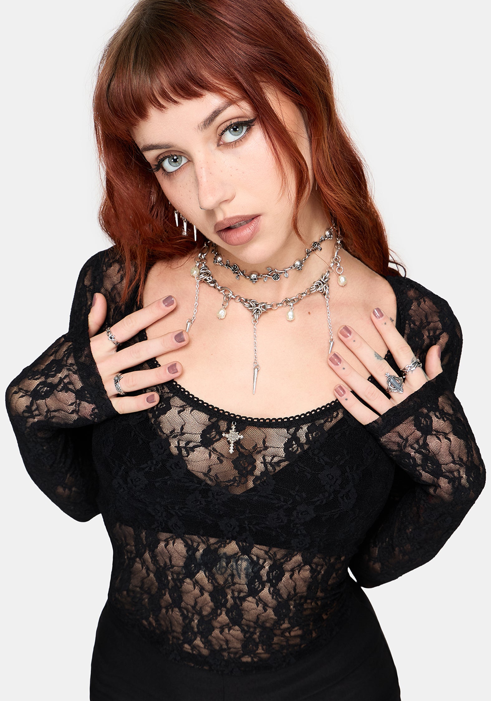 Woman wearing a black lace top with layered necklaces on a white background