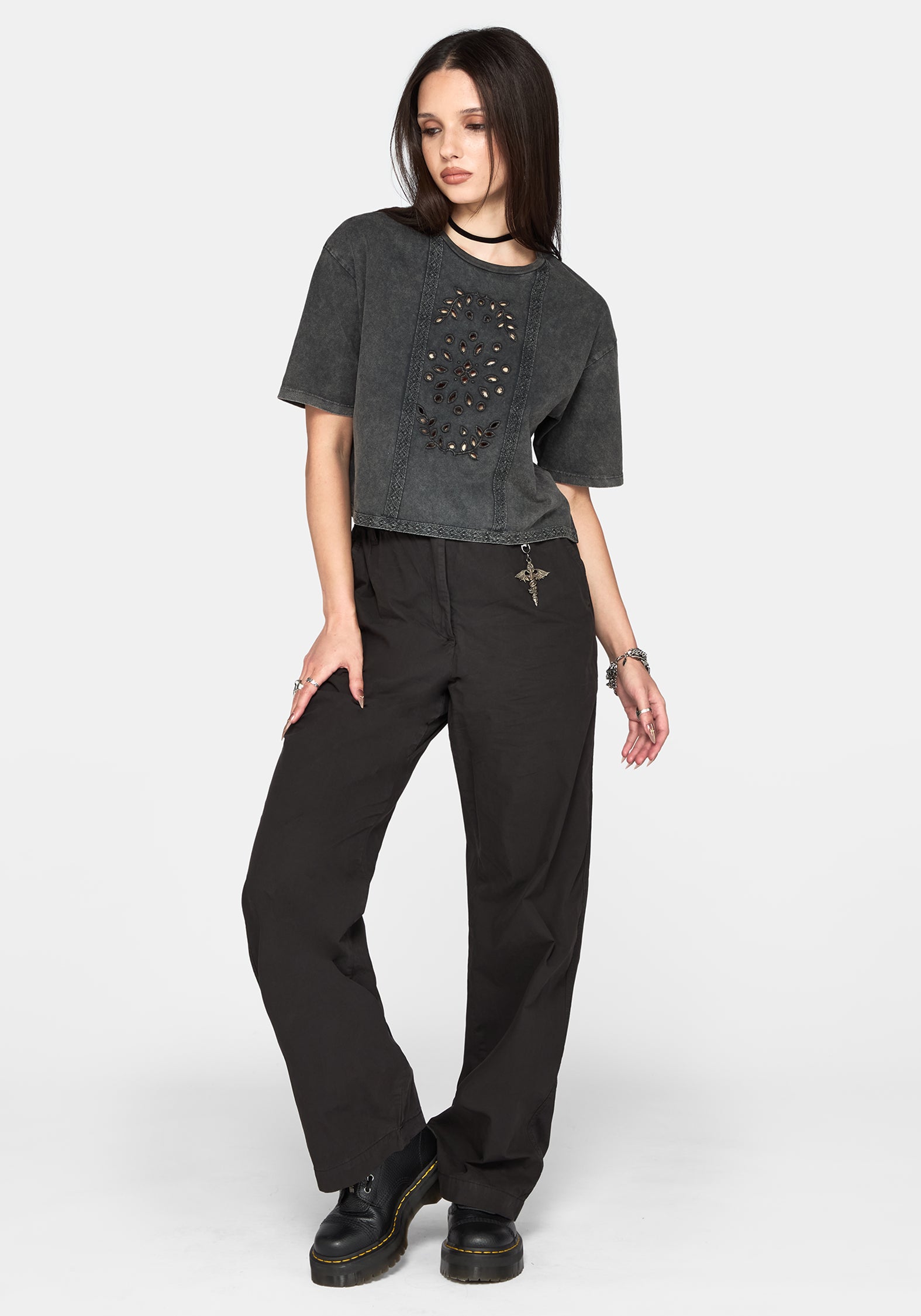 A model wearing a washed black cropped t-shirt with a skull graphic and black wide-leg pants, standing against a light gray studio background.