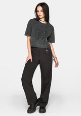 A model wearing a washed black cropped t-shirt with a skull graphic and black wide-leg pants, standing against a light gray studio background.