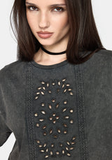 A close-up of a woman wearing a dark gray textured top with a circular cutout pattern on the chest and a black choker necklace.
