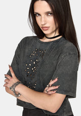 A woman wearing a dark grey washed short-sleeve crop top with cutout details on the front, styled with a black choker and silver bracelets against a light gray background.