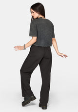 A woman posing from the back wearing a dark grey cropped t-shirt and black wide-leg trousers against a light gray background.
