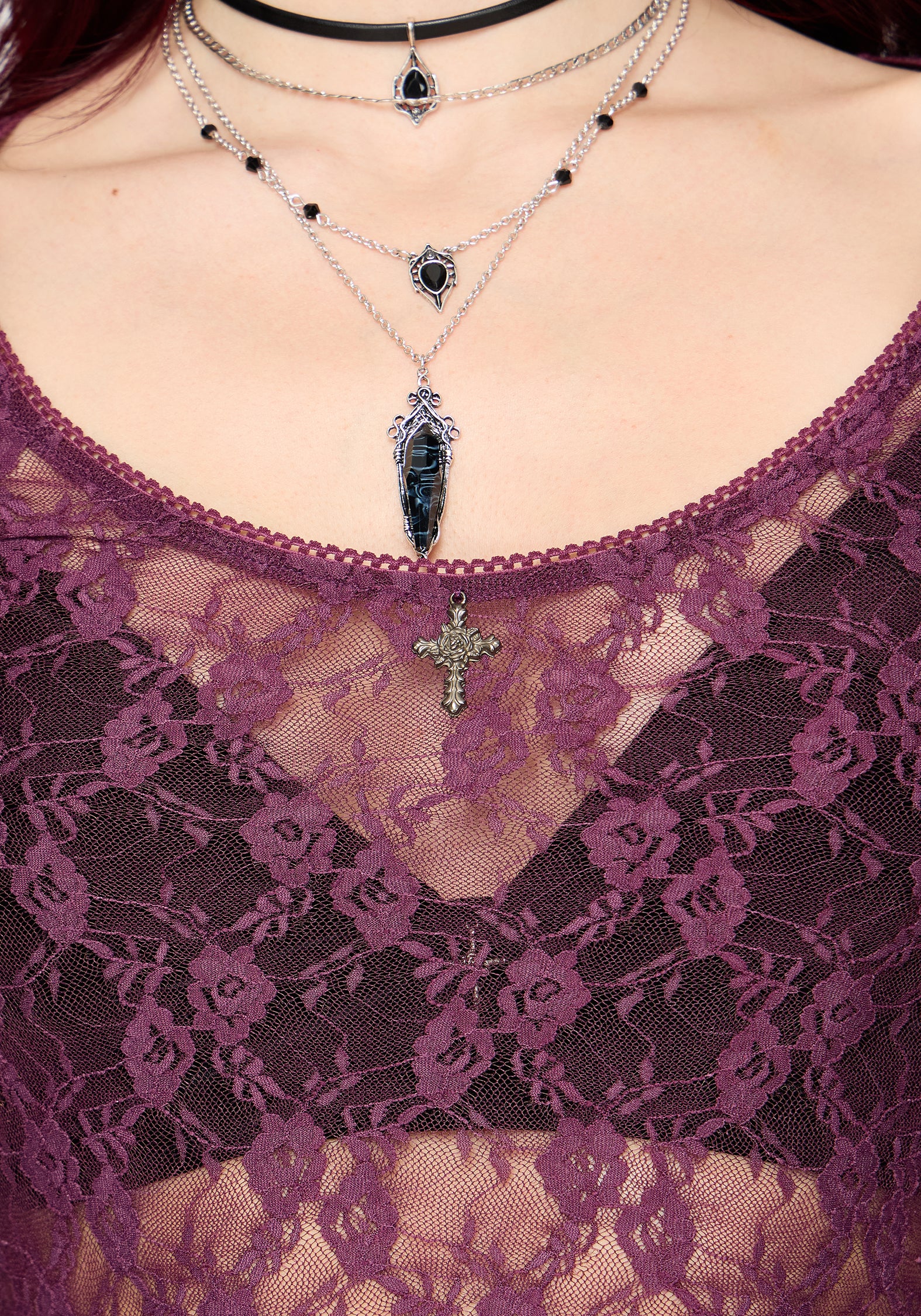 Close-up of a person wearing layered necklaces with a purple lace top.