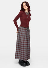 A woman wearing a ribbed long-sleeve button-front knit top in deep burgundy, paired with a gray and burgundy plaid skirt and layered silver chain necklaces, against a light gray studio background.