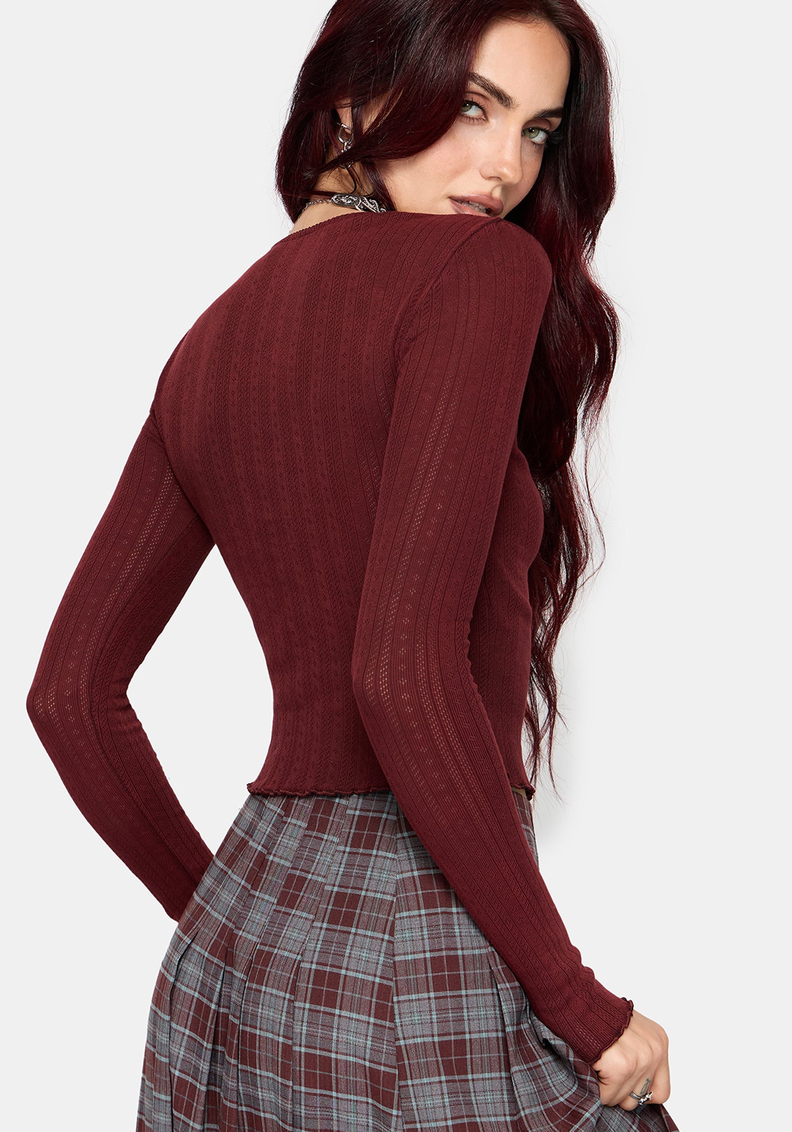 A woman wearing a ribbed long-sleeve knit top in deep burgundy, paired with a gray and burgundy plaid skirt, shown from a three-quarters back view against a light gray background.