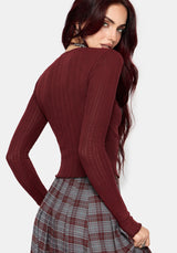 A woman wearing a ribbed long-sleeve knit top in deep burgundy, paired with a gray and burgundy plaid skirt, shown from a three-quarters back view against a light gray background.
