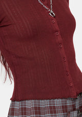 A close-up of a ribbed knit top in deep burgundy, featuring a button-down front and a silver chain necklace, paired with a plaid skirt.