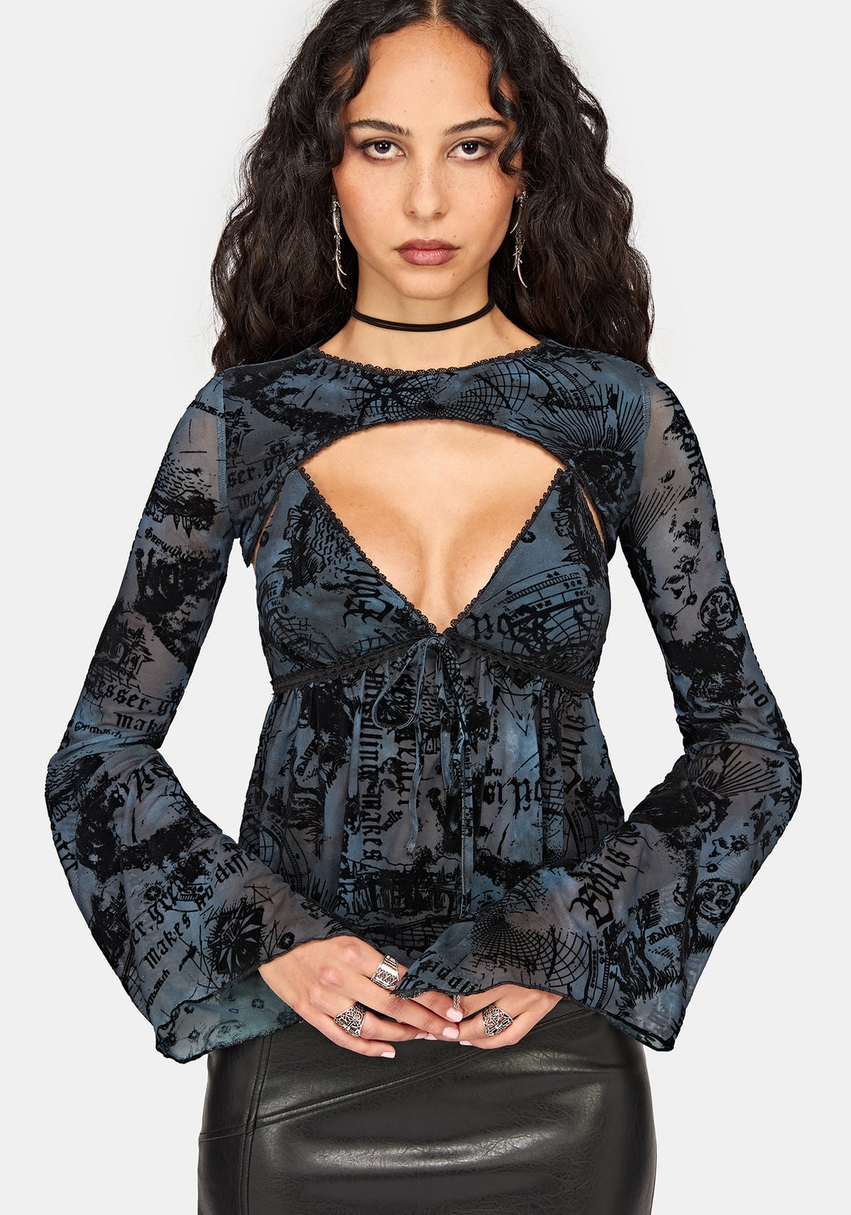 A woman modeling a black and blue patterned camisole top with thin straps and a ruffled peplum, paired with a black faux-leather skirt, against a light gray background.