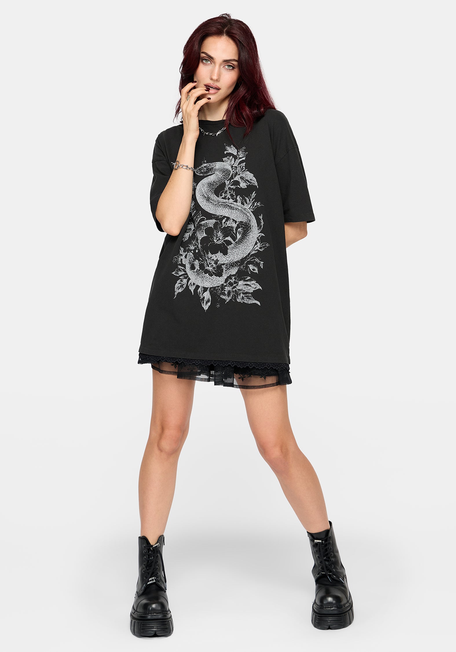 A model with dark red hair wearing an oversized black t-shirt dress featuring a large white dragon graphic on the front, styled with black lace-up combat boots against a light gray background.