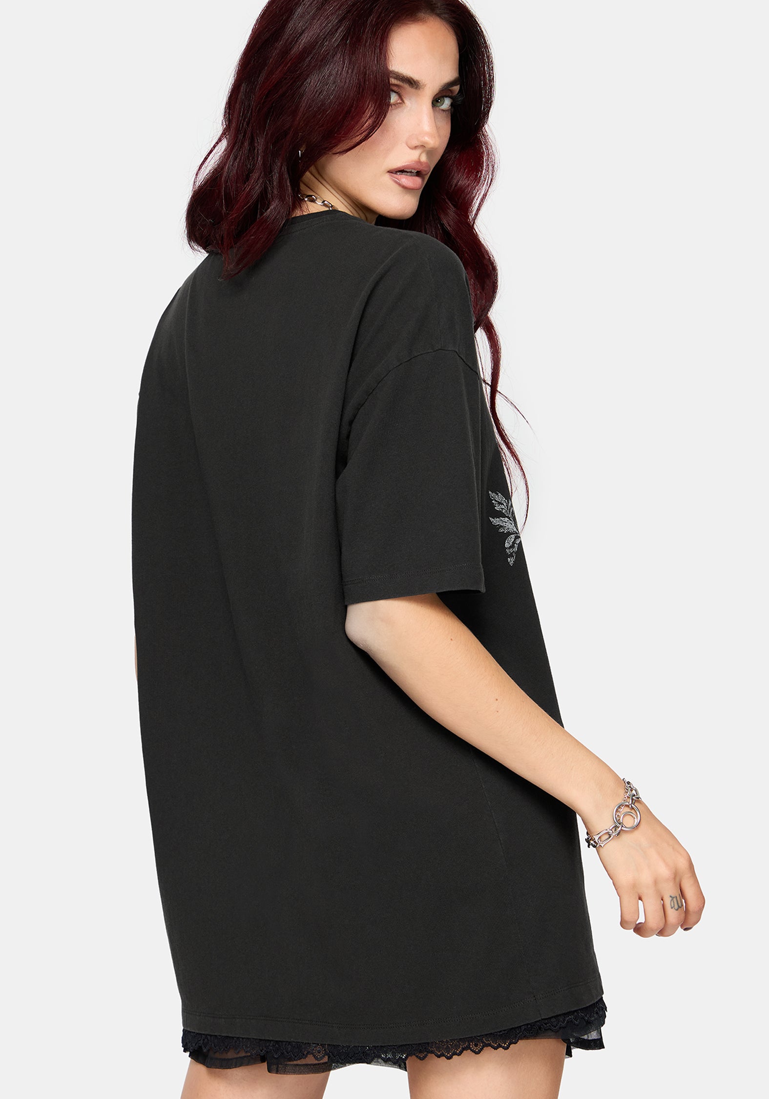A woman modeling an oversized black t-shirt with a large white graphic print of a coiled snake and floral elements on the front, set against a plain light gray background.
