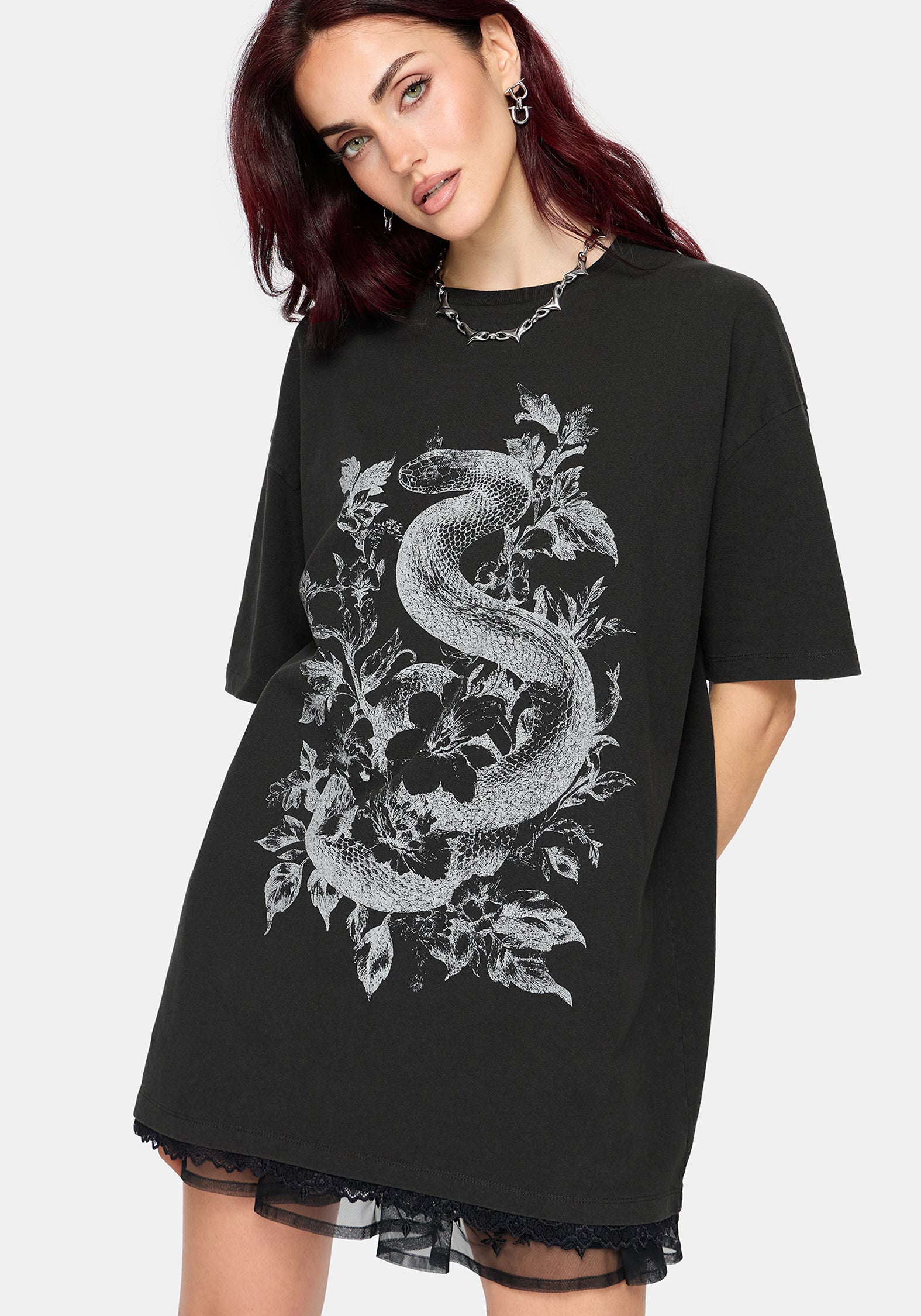 A woman wearing an oversized black t-shirt dress with a large white snake and floral graphic on the front, paired with a sheer black lace hem.