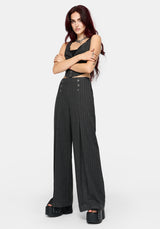 A model with dark red hair stands against a light gray studio background wearing a grey pinstriped crop top and matching high-waisted, wide-leg trousers with button details at the hips, paired with black platform sandals.