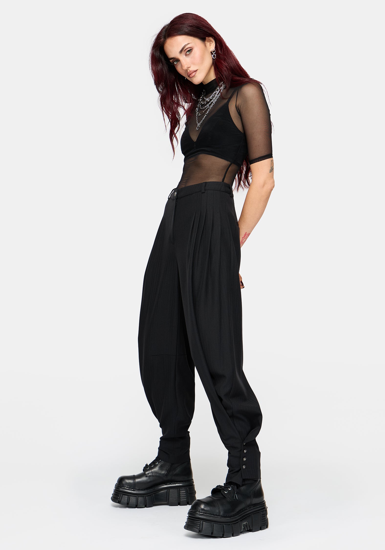 A model wearing a black sheer mesh short-sleeve crop top and matching black balloon pants with cuffs, styled with chunky black platform boots against a light gray background.