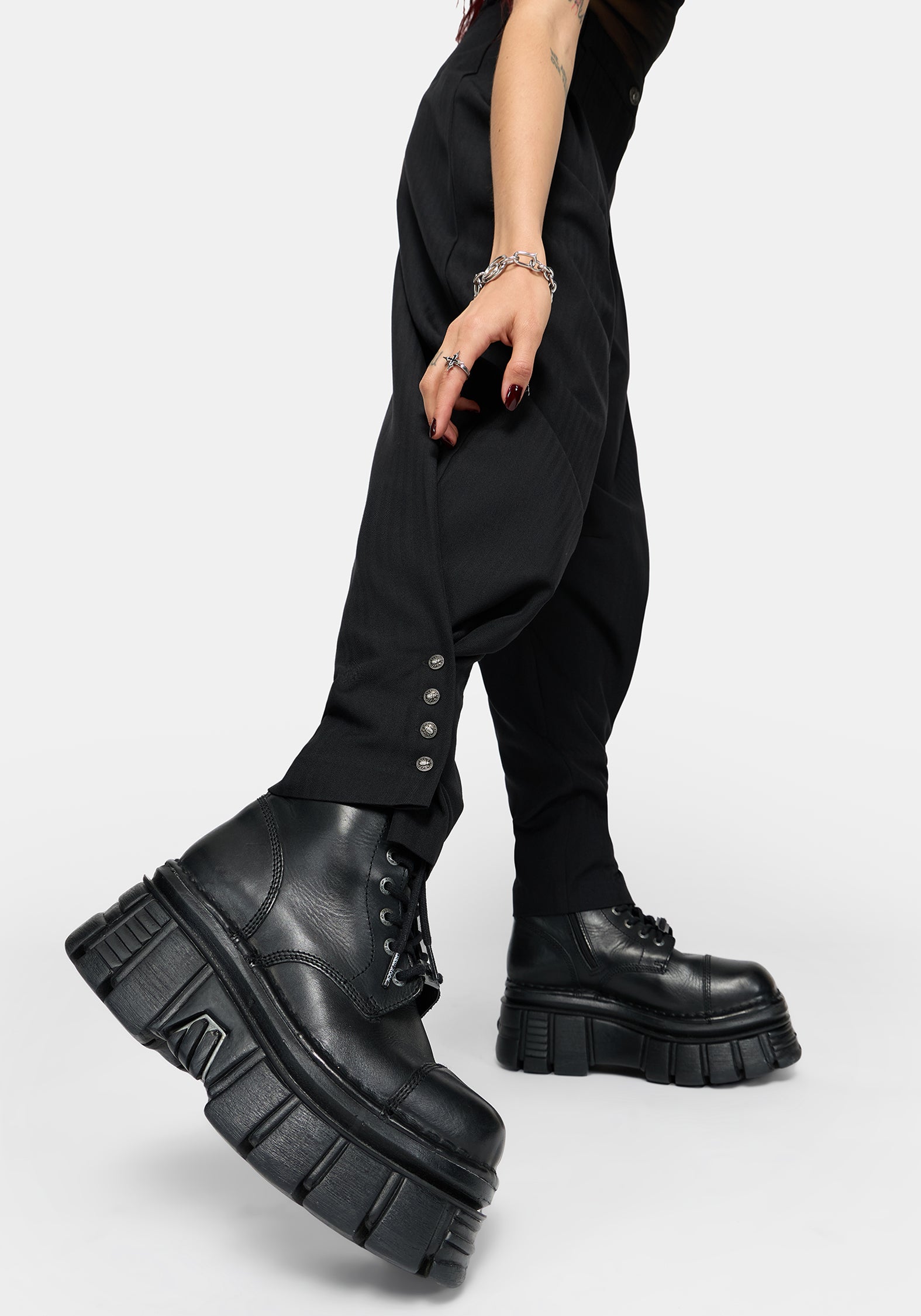 A person wearing black balloon pants with decorative silver buttons at the cuffs and chunky black platform lace-up boots, shown against a light gray studio background.