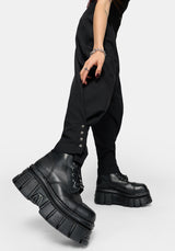 A person wearing black balloon pants with decorative silver buttons at the cuffs and chunky black platform lace-up boots, shown against a light gray studio background.