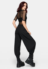 A model wearing a black sheer mesh short-sleeve crop top and matching black balloon pants with cuffs, styled with chunky black platform boots against a light gray background.