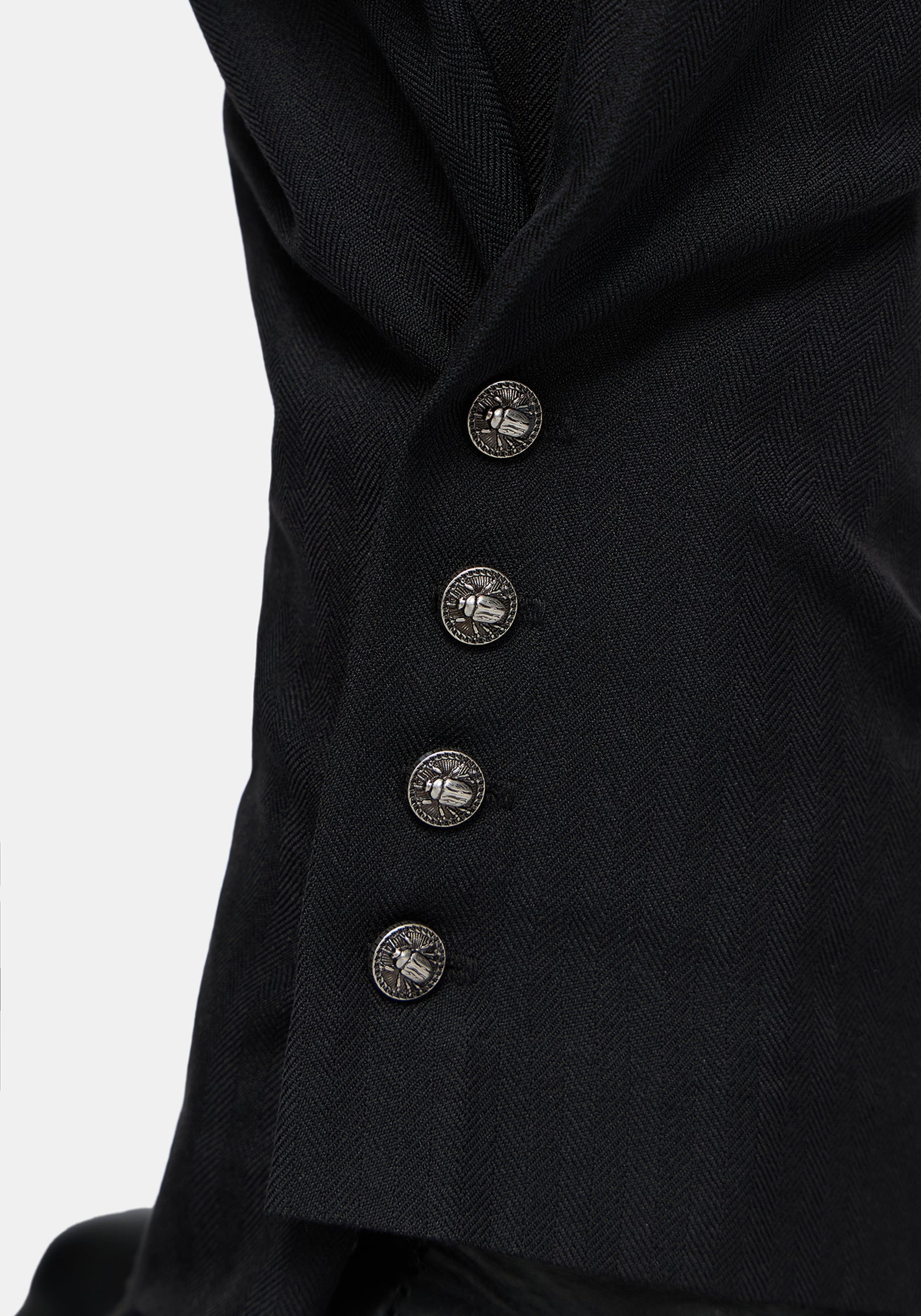Close-up of black balloon trousers   with four decorative metallic buttons on a light gray background.